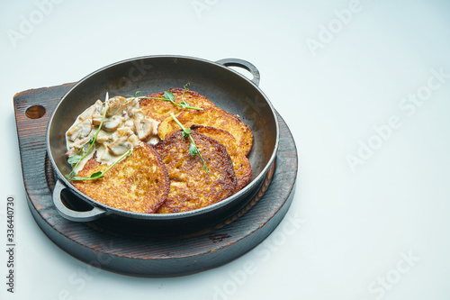 Close up view on Traditional dish of Ukrainian cuisine - potato pancakes with sour cream and mushroom in frying pan isolated on grey background