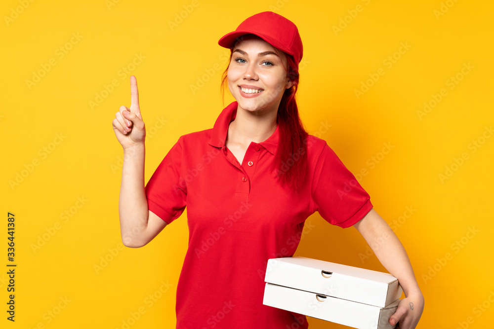 Pizza delivery girl holding a pizza over isolated background showing and lifting a finger in sign of the best Pizza delivery girl holding a pizza over isolated background showing and lifting a finger in sign of the best