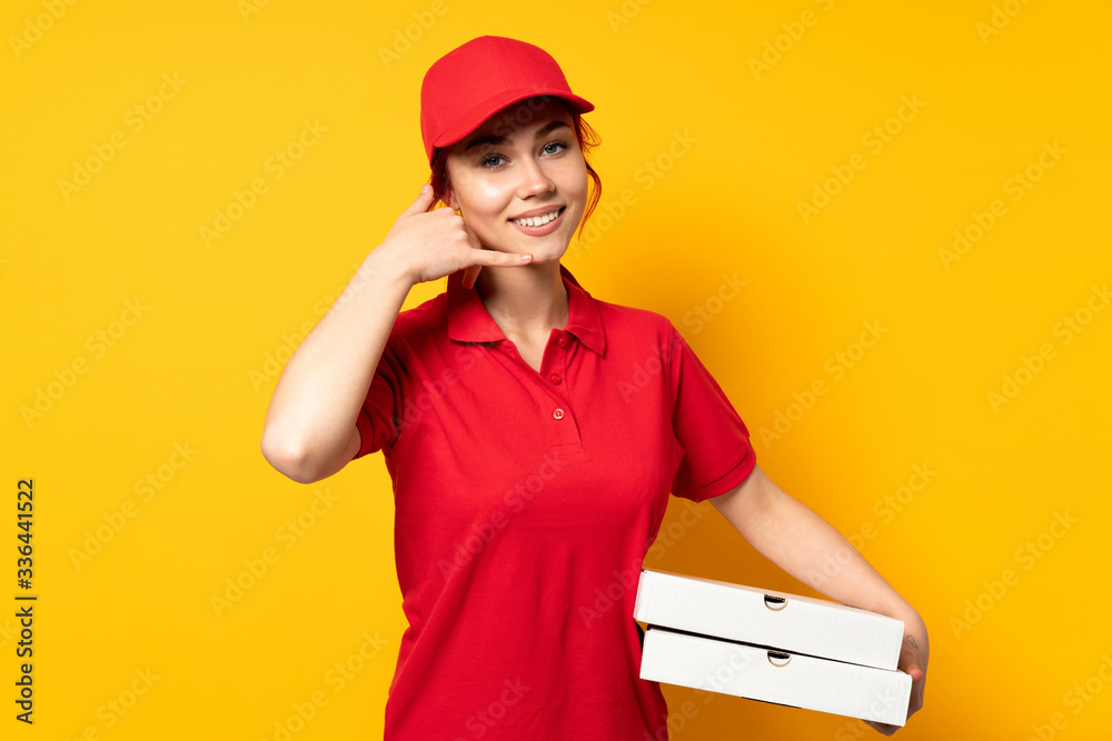 Pizza delivery girl holding a pizza over isolated background making phone gesture and pointing front Pizza delivery girl holding a pizza over isolated background making phone gesture and pointing front