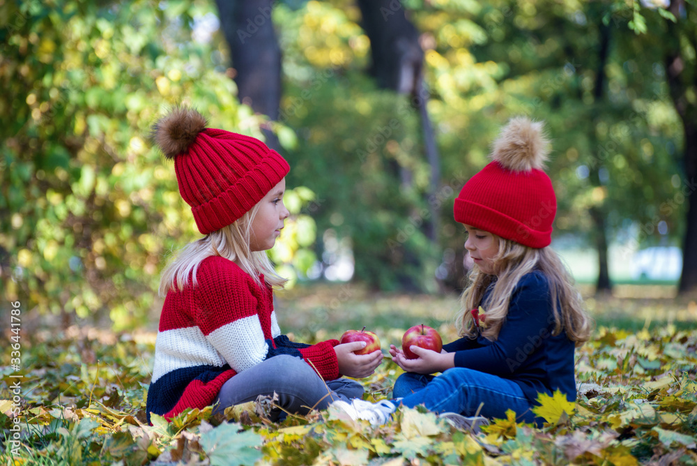 Two cute little sisters eating apples in the park Two cute little sisters eating apples in the park