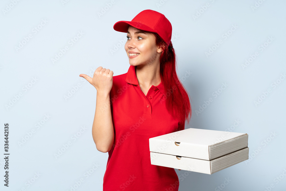 Pizza delivery girl holding a pizza over isolated background pointing to the side to present a product Pizza delivery girl holding a pizza over isolated background pointing to the side to present a product