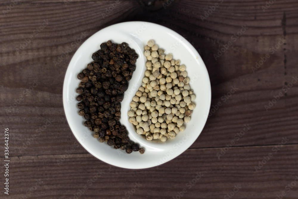 Black and white pepper corns in Yin Yang shaped bowl on wooden background Black and white pepper corns in Yin Yang shaped bowl on wooden background