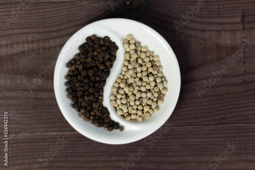 Black and white pepper corns in Yin Yang shaped bowl on wooden background