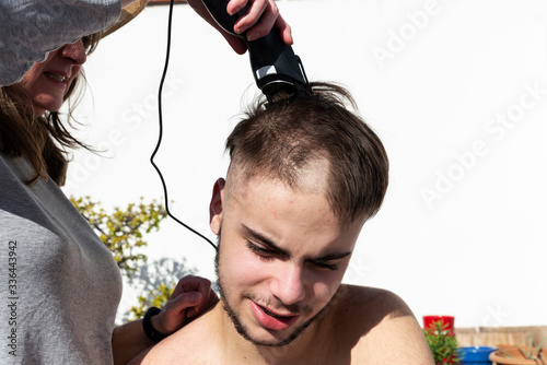 Mother cutting the hair of a teenager with hair clipper
