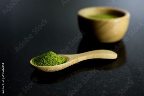 Matcha green tea powder in wooden bowl and spoon on black background.