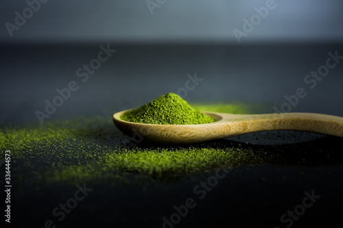 Matcha green tea powder on wooden spoon on black background.
