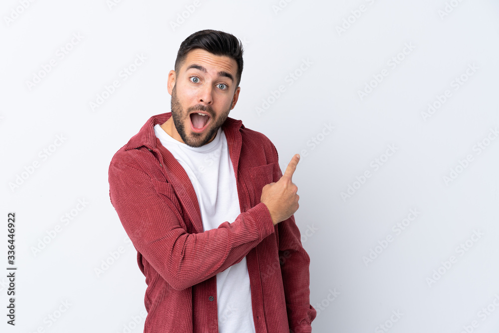 Young handsome man with beard wearing a corduroy jacket over isolated white background surprised and pointing side Young handsome man with beard wearing a corduroy jacket over isolated white background surprised and pointing side