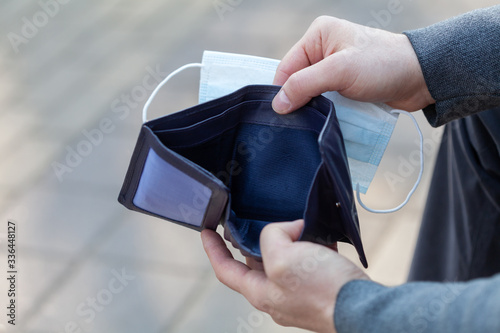 Obraz na plátne Man holds a medical mask and empty wallet without money