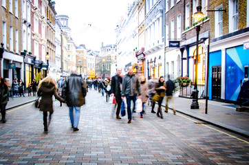 Motion blurred people on busy city street of shops