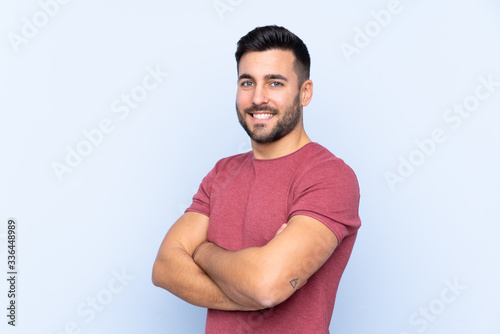 Young handsome man with beard over isolated blue background with arms crossed and looking forward
