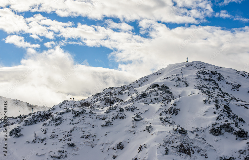 Obraz premium Two people climbing a snow covered mountain towards a cross on the top