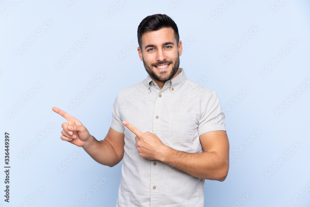 Young handsome man with beard over isolated blue background pointing finger to the side Young handsome man with beard over isolated blue background pointing finger to the side