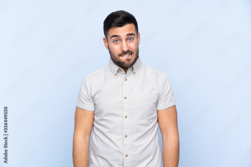 Young handsome man with beard over isolated blue background having doubts and with confuse face expression Young handsome man with beard over isolated blue background having doubts and with confuse face expression