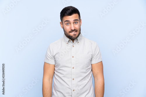 Young handsome man with beard over isolated blue background having doubts and with confuse face expression
