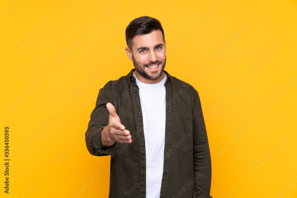 Man over isolated yellow background handshaking after good deal Man over isolated yellow background handshaking after good deal
