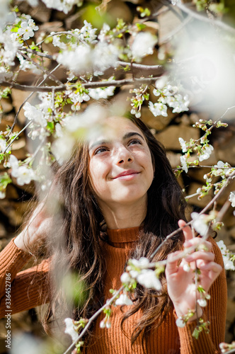 Spring girl near tree sniffing white flowers