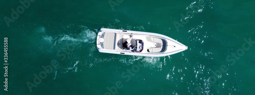 Aerial drone top down ultra wide photo of white speedboat cruise in low speed in emerald clear water lake