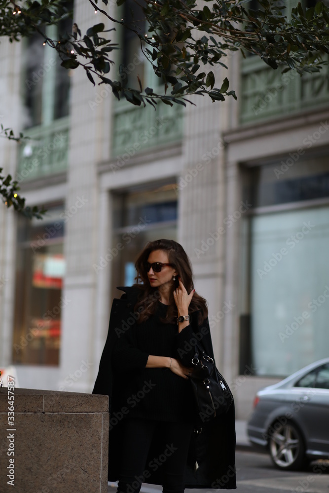 Fototapeta premium A beautiful woman in a black long coat walks through the streets of New York