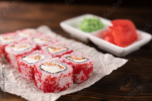rolls with red fish, caviar and cheese on paper on a dark wooden board close up