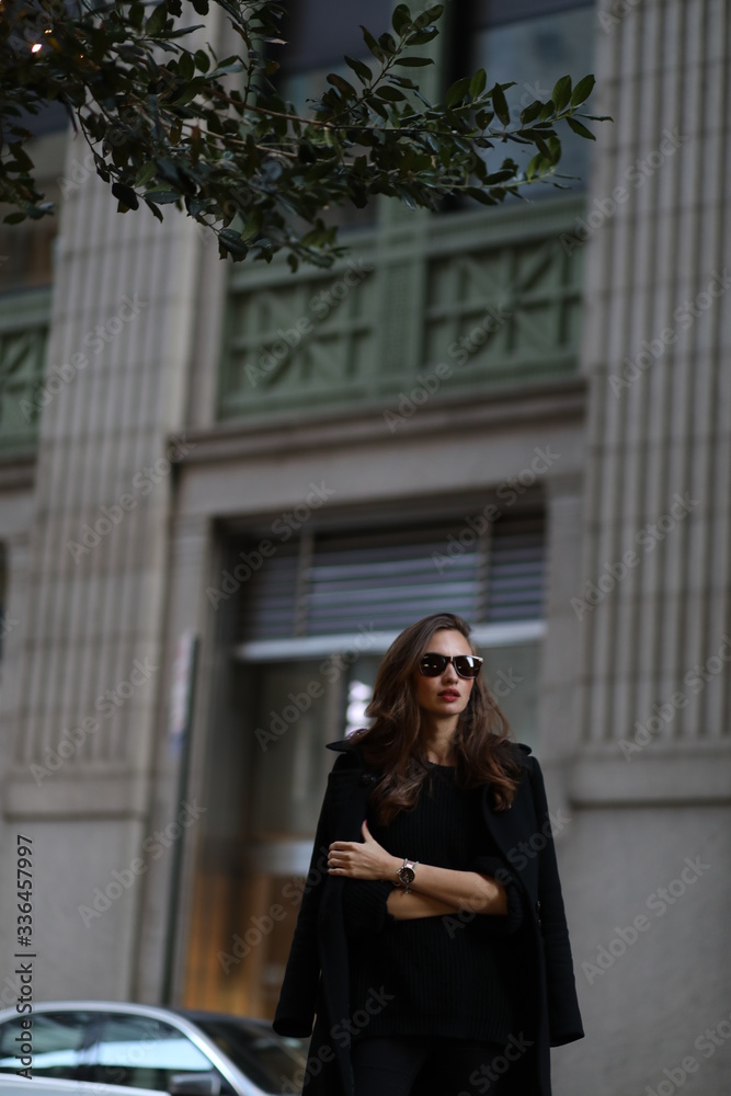 Naklejka premium A beautiful woman in a black long coat walks through the streets of New York