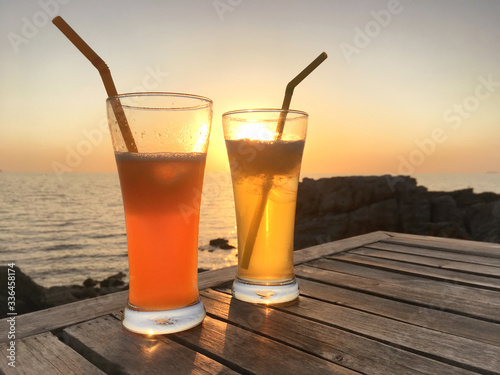 Frozen cocktail glasses with straws on wooden table over sea sunset