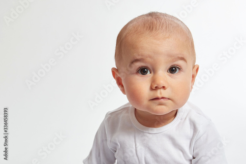 Fototapeta A baby boy looks into camera wearing a white shirt on a white background
