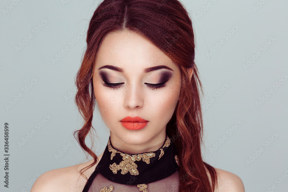 Just beautiful. Close up of a gorgeous woman red lips, black long eyelashes full makeup clean skin  eyes closed curly hair up isolated on a light gray green background wall