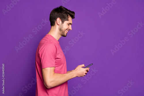 Side profile view photo of satisfied glad positive user holding telephone in hands enjoying good news on the internet isolated violet background