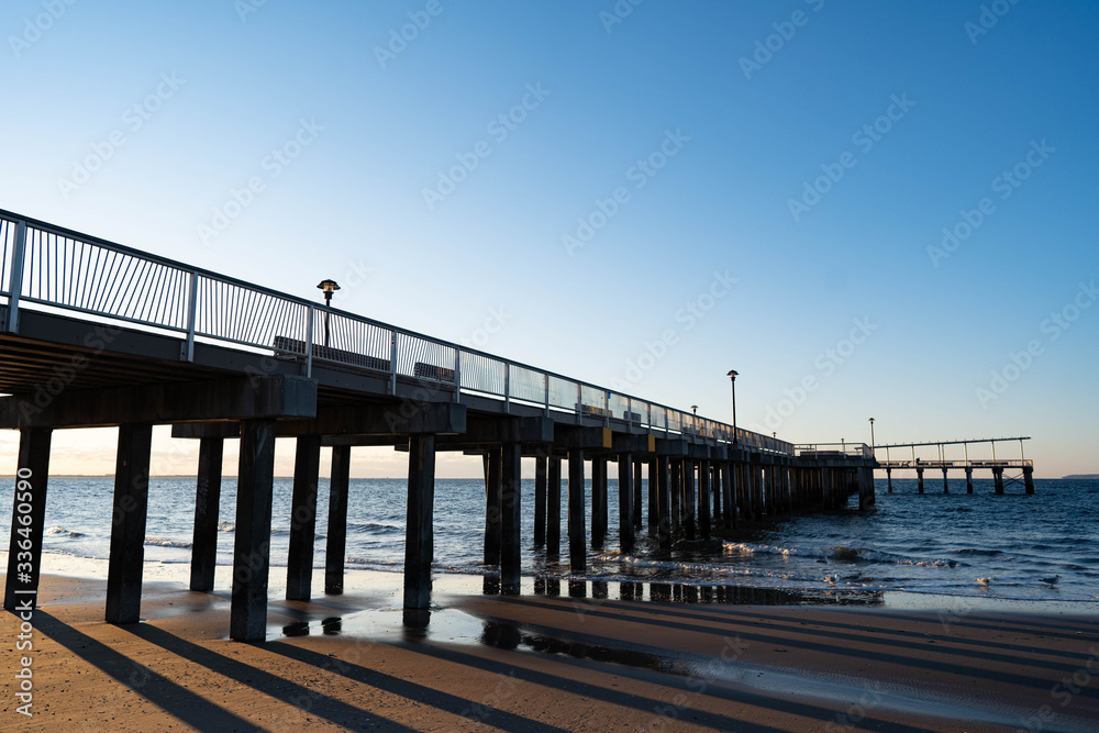 Sunrise over Atlantic Ocean with blue clear sky, blue ocean, wooden pier, birds flying over sunrise red sky beams

