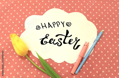 Photo of white paper in the shape of cloud on pink polka dot fabric. Happy Easter - lettering. Color abstract mockup background template with pen pencil marker bunny flower tulip