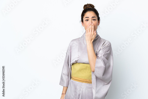 Woman wearing kimono over isolated background covering mouth with hand