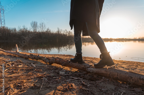 Young girl walking on the log by the beach of a lake during sunset
