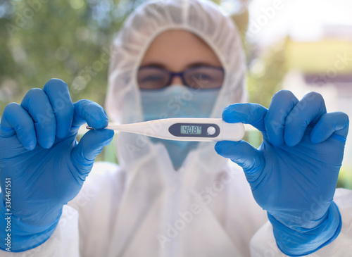 Medical worker in protective suit and mask holding thermometer