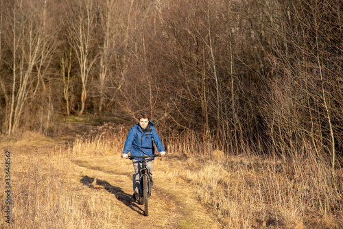 A teenager rides a Bicycle on dry grass against a background of bare trees. Early spring landscape. © FO_DE