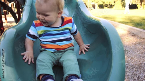 Front view of toddler joyfully sliding down playground slide summer afternoon