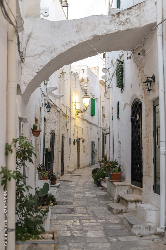 Narrow street in the old white town of italian  Ostuni with flowers, arc and streetlight