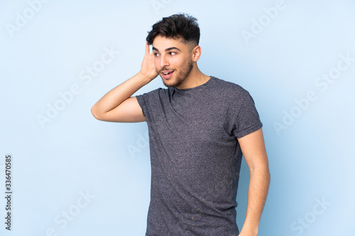 Arabian handsome man over isolated background listening to something by putting hand on the ear