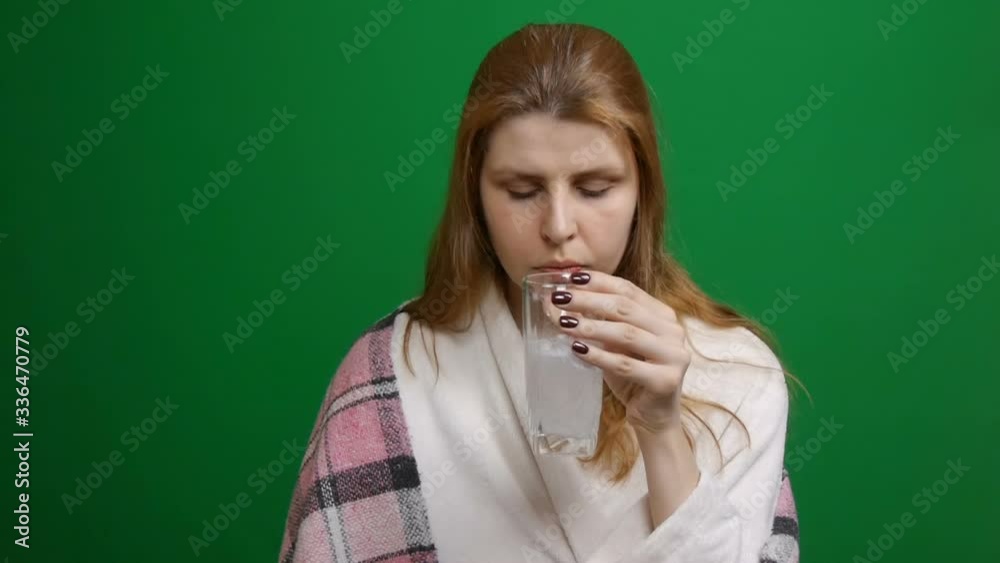 Woman is drinking an effervescent pill. The pill drops and dissolves with bubbles. Red hair. COVID Effervescent tablet in a glass of water on a green background. Woman is drinking an effervescent pill. The pill drops and dissolves with bubbles. Red hair. COVID Effervescent tablet in a glass of water on a green background.