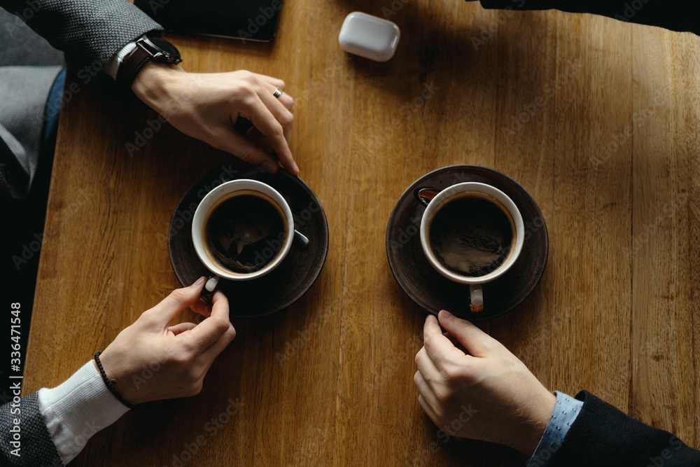 Top view two men hands gesticulating while holding cups of coffee on a wooden table background