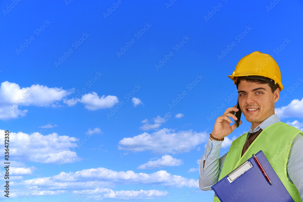 Young engineer with helmet and clipboard, speaking on mobile phone Young engineer with helmet and clipboard, speaking on mobile phone