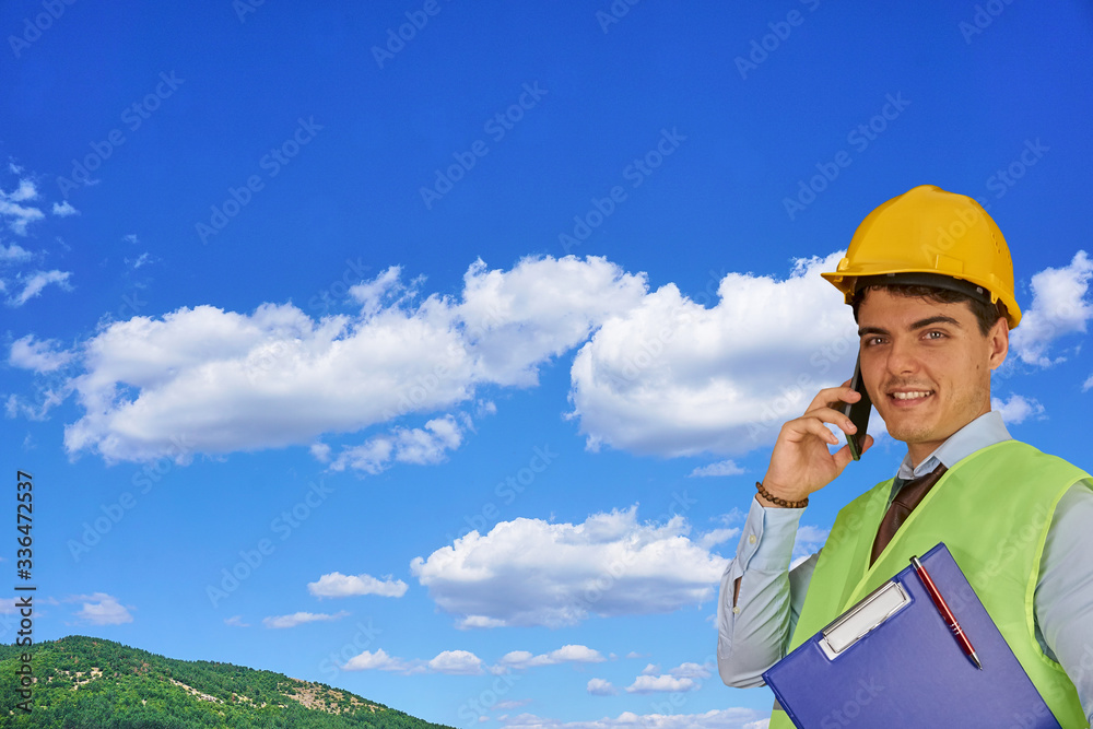 Young engineer with helmet and clipboard, speaking on mobile phone Young engineer with helmet and clipboard, speaking on mobile phone