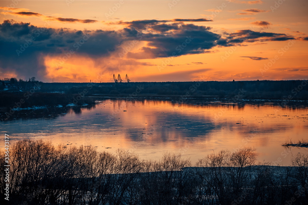 the setting sun beautifully illuminates cumulus clouds slowly floating over a full-flowing river on a warm spring evening the setting sun beautifully illuminates cumulus clouds slowly floating over a full-flowing river on a warm spring evening