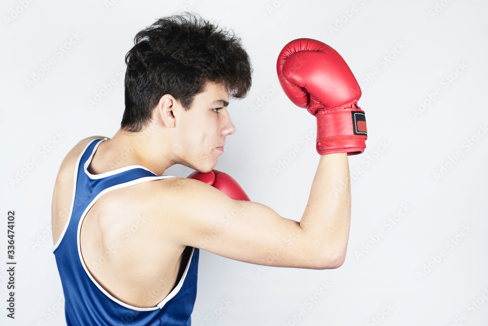 Young teenage boy boxing on light background. A teenager in boxing gloves trains a kick from below - an uppercut. A boy has a focused look Young teenage boy boxing on light background. A teenager in boxing gloves trains a kick from below - an uppercut. A boy has a focused look