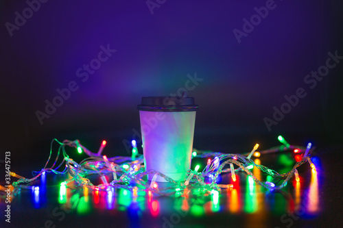 Takeaway paper cup on black background surrounded by light bulbs.