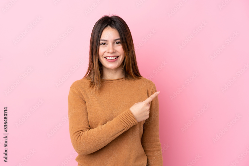 Obraz premium Young woman over isolated pink background surprised and pointing side