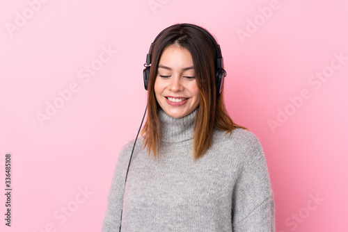 Young woman listening music with headphones over isolated pink wall