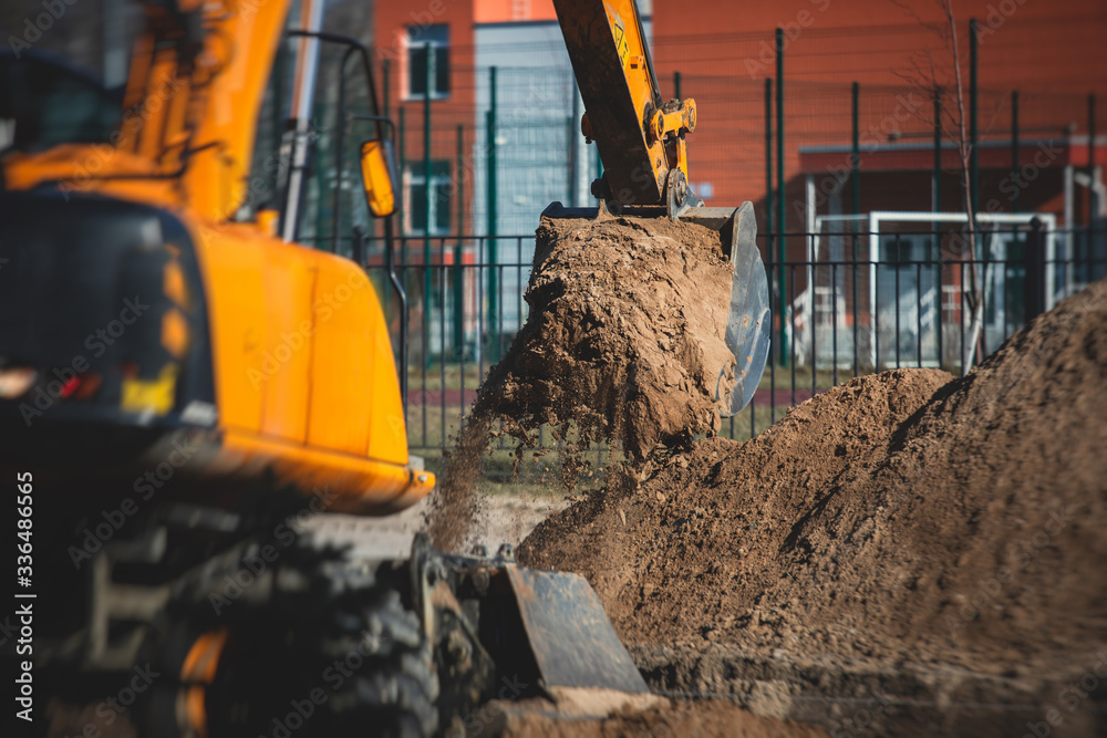 Fototapeta premium Yellow heavy excavator excavating sand and working during road works, unloading sand during construction of the new road with workers around