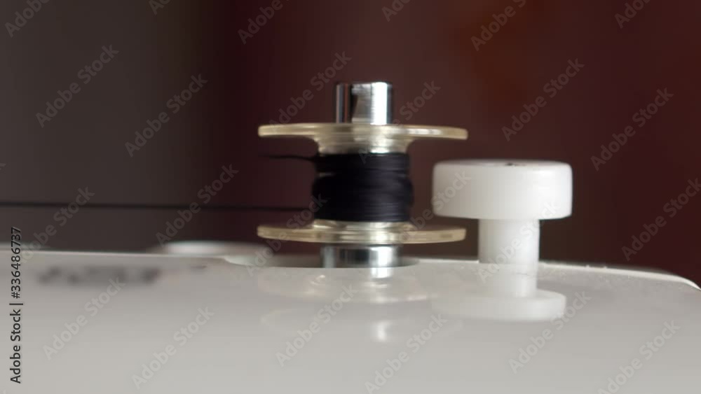 Winding a black thread on a small spool. Close-up of automatic thread winding on an empty sewing machine bobbin Winding a black thread on a small spool. Close-up of automatic thread winding on an empty sewing machine bobbin