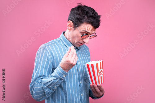 Side view of serious young man look inside small empty bucket of popcorn. Nothing to eat. Isolated over pink background.