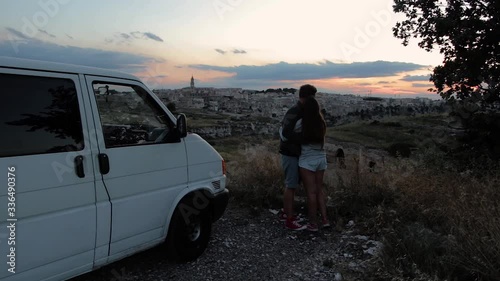 young adventure couple watching the sunset over an old cavetown while cuddeling. Campervan in the back photo